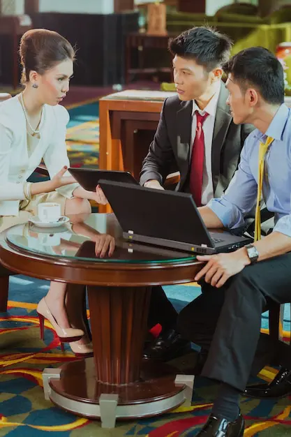Leoker business consultants engaging in a strategic discussion with client, reviewing market data on laptops while providing professional advisory services in a business meeting setting
