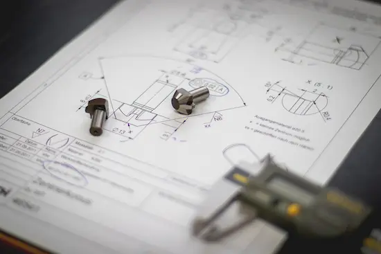Close-up of a technical drawing with precision bolts and a caliper, representing leoker's production inspection and quality assurance services for maintaining client and industry standards.